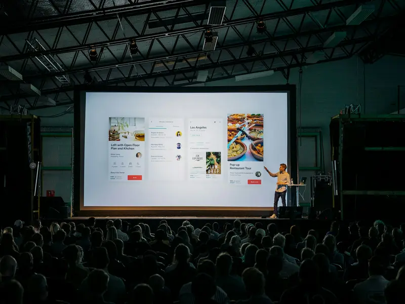 A speaker addressing a hall in front of a large presentation screen