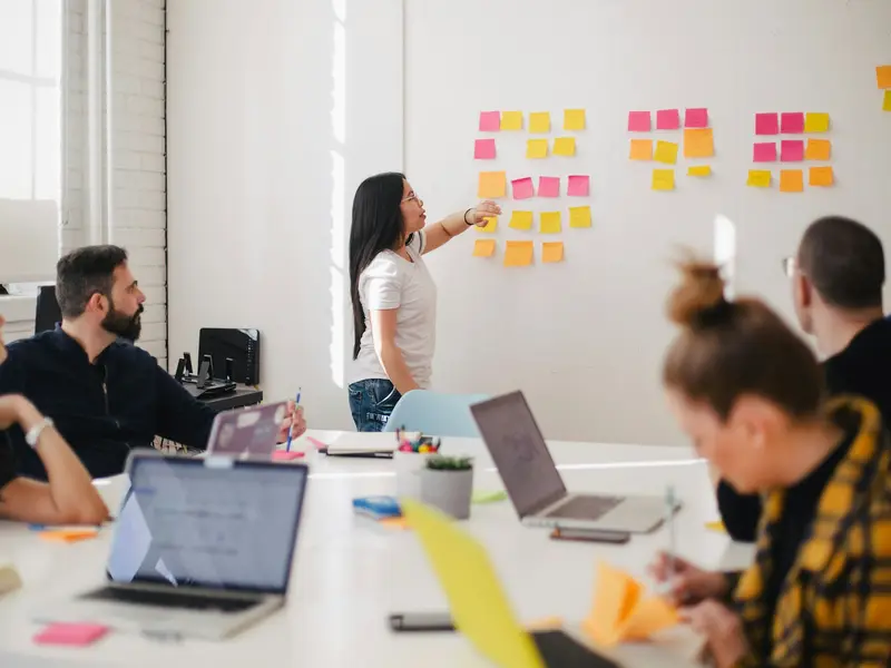 A workshop host putting sticky notes on a board while people work at the table
